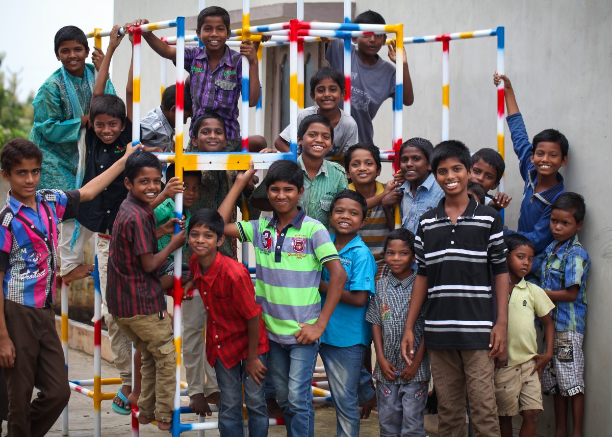 a group of boys from Children of Faith are climbing on a play structure.