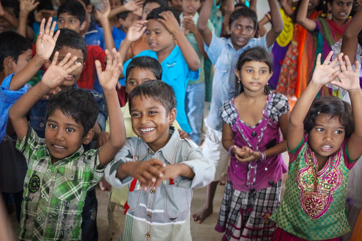 a group of young children at Children of Faith singing with hands in the air