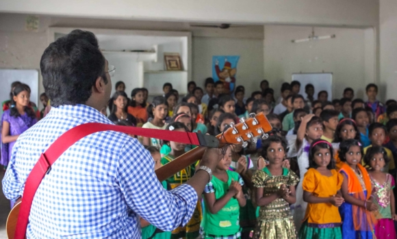 man with guiatr sining to group of children