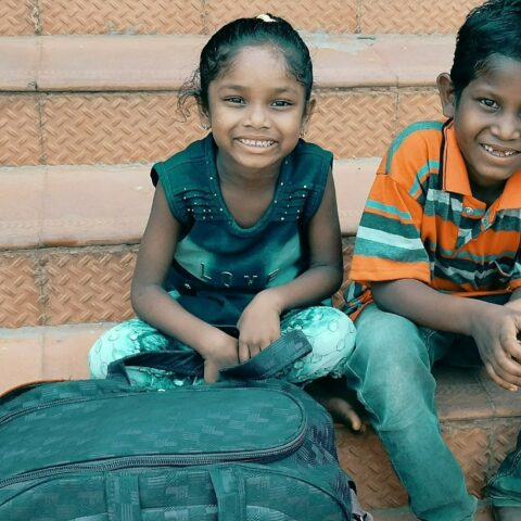 Two children waith on the steps with their bags