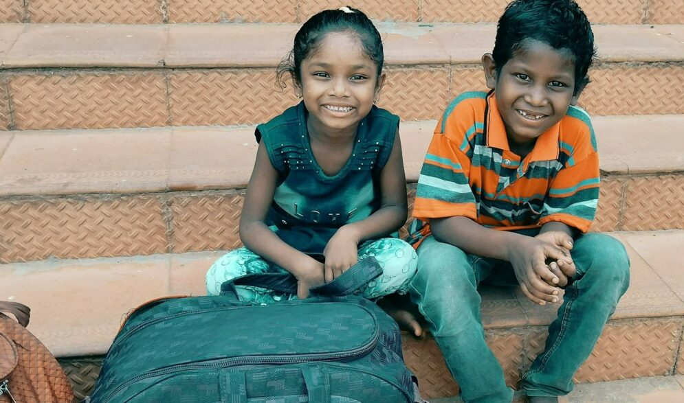 Two children waith on the steps with their bags