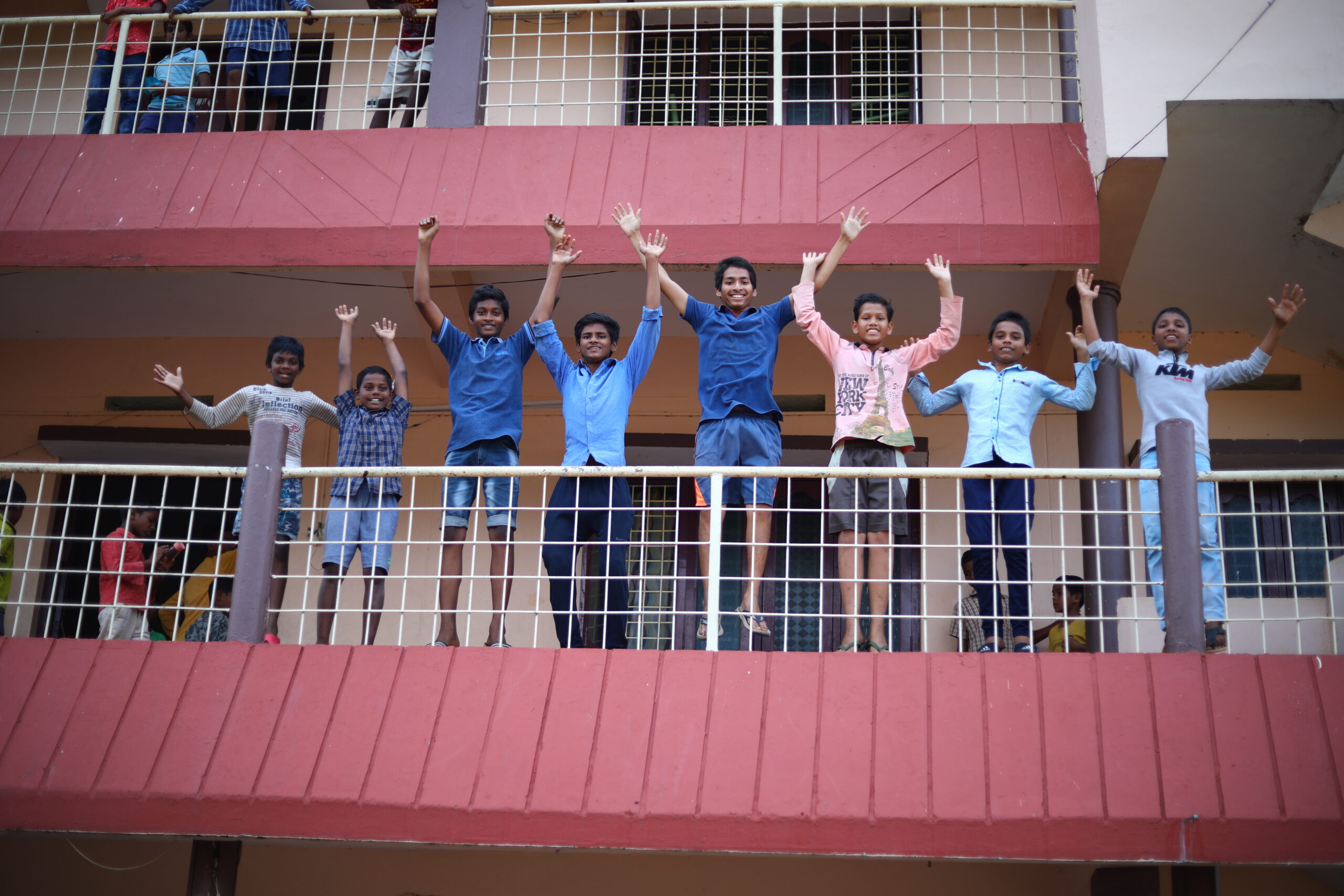 Young boys on a balcony raise thier arms to celebrate the opportunites they have thanks to Children of Faith