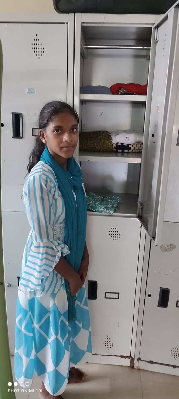 Young girl sorts her clothing into a locker at the Children of Faith Home in India