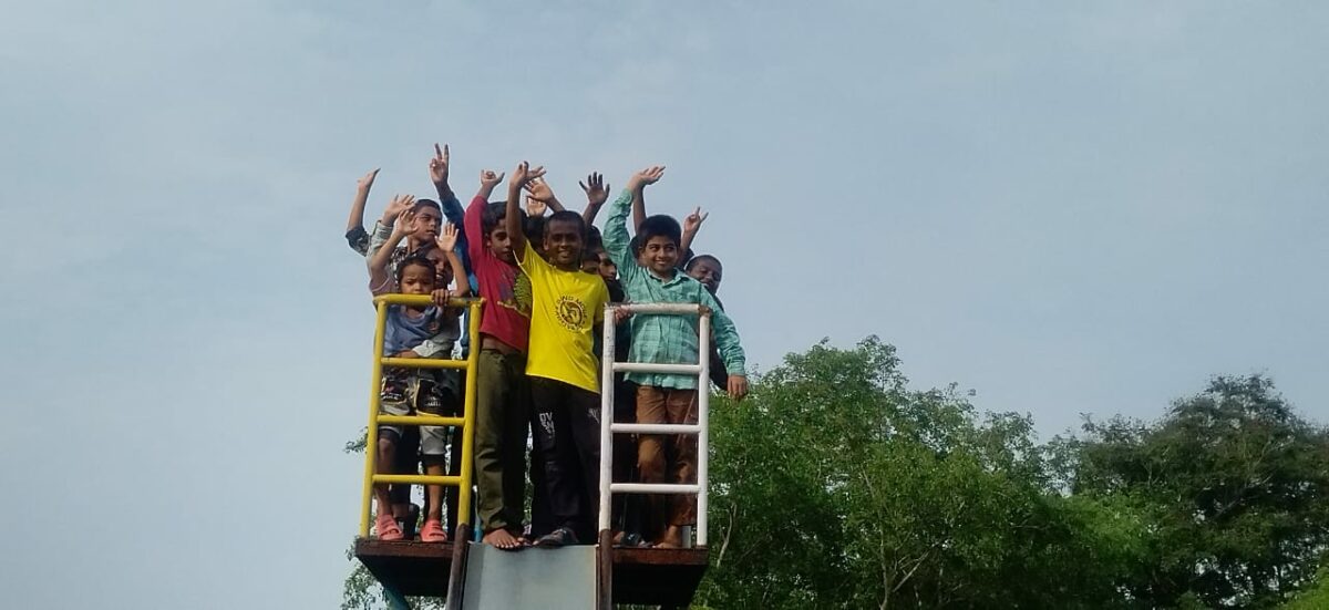 Boys from Children of Faith wave from the top of the slide at the park